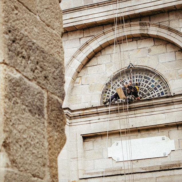 Hombre con arnés restaurando vidriera sobre fachada de piedra